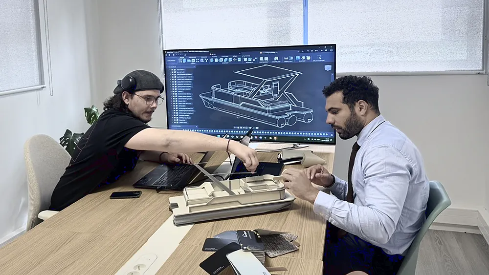Deux membres de l'équipe Lounge Cruise autour d'une maquette de ponton, le modèle 3D du bateau affiché à l'écran